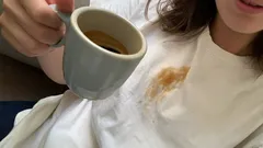 Macchia di caffè su maglietta bianca mentre una persona tiene una tazza in mano.