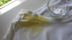 Macchia gialla su maglietta bianca con ciotola di bicarbonato per rimozione macchie.