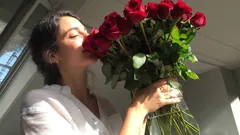 Donna che annusa un grande mazzo di rose rosse in una stanza luminosa