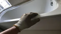Manutenzione vasca da bagno con mano guantata vicino al bordo in bagno luminoso