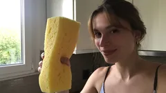 Donna in cucina tiene in mano una grande spugna gialla per pulizie domestiche.