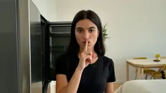 Donna fa gesto silenzio in cucina, frigorifero aperto, atmosfera domestica.
