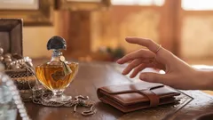 Profumo elegante su tavolo antico con mano e portafoglio, atmosfera raffinata.