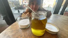 Vaso di miele con cannuccia su tavolo di legno, donna sfocata sullo sfondo