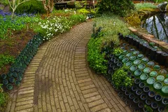 Sentiero in mattoni in giardino con bordure di bottiglie di vetro verdi e fiori colorati.