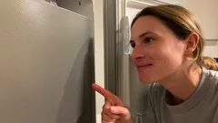 Donna sorride e punta il dito verso frigorifero aperto in cucina.